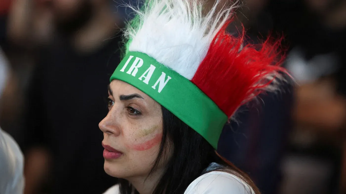 امرأة ترتدي قبعة رياضية تحمل ألوان علم إيران، تعبر عن دعمها للمنتخب الإيراني في مباراة كأس العالم، وسط أجواء حماسية.