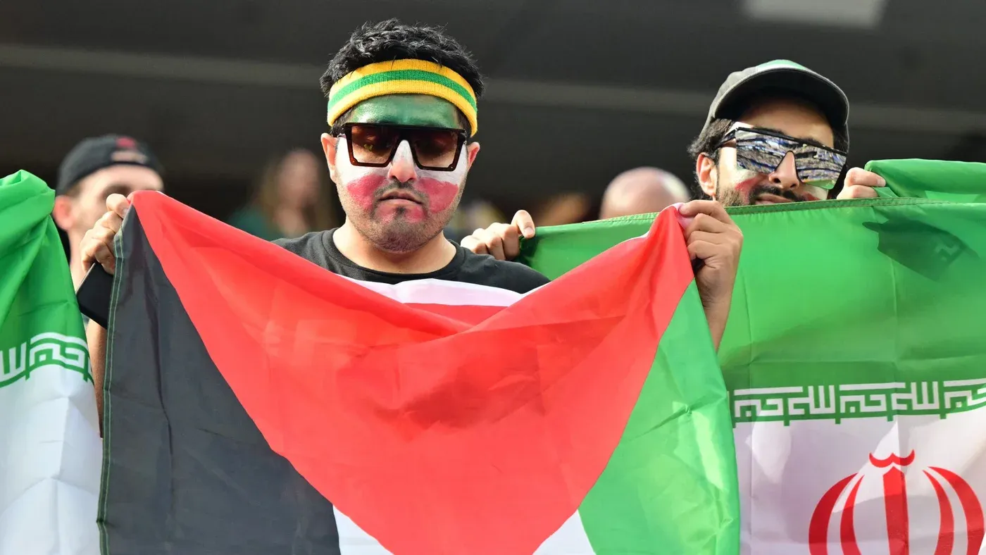 مشجعون برسم وجوههم ويرفعون العلم الفلسطيني إلى جانب العلم الإيراني في مدرجات كأس العالم تضامناً مع فلسطين.