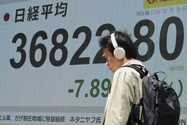 شخص يسير بجوار شاشة تعرض مؤشر نيكاي 225 الياباني، مع انخفاض قدره 7.89 نقطة، مما يعكس تقلبات السوق.