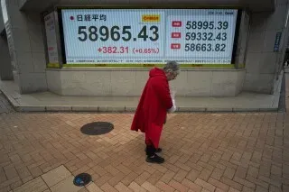 امرأة ترتدي معطفًا أحمر تسير بجانب شاشة تعرض مؤشرات سوق الأسهم الياباني نيكاي 225، التي تظهر ارتفاعًا ملحوظًا.