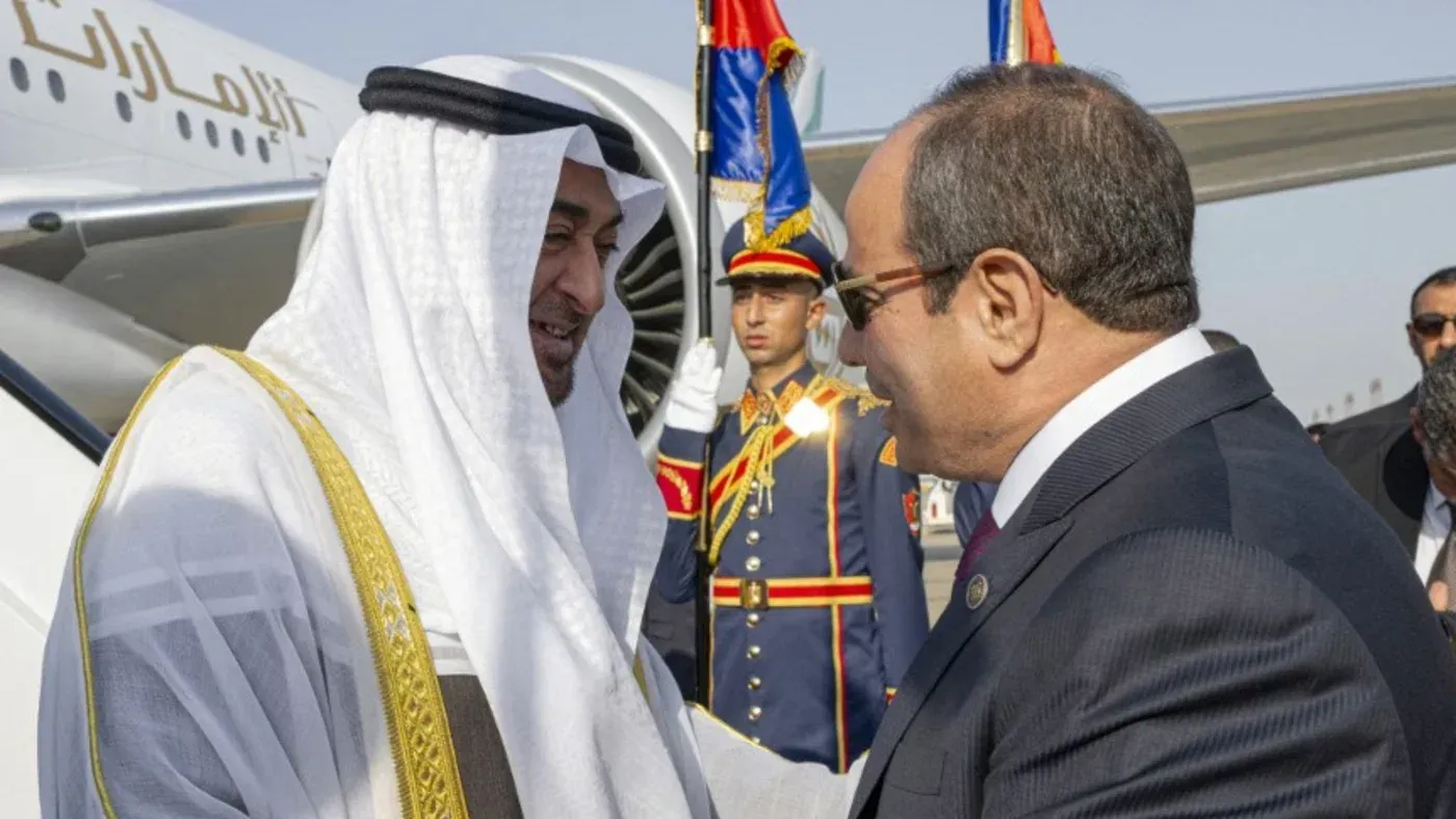 لقاء بين الرئيس المصري عبد الفتاح السيسي وولي عهد الإمارات، مع خلفية من الجنود والرايات، يعكس التعاون الإقليمي في ظل التوترات السياسية.