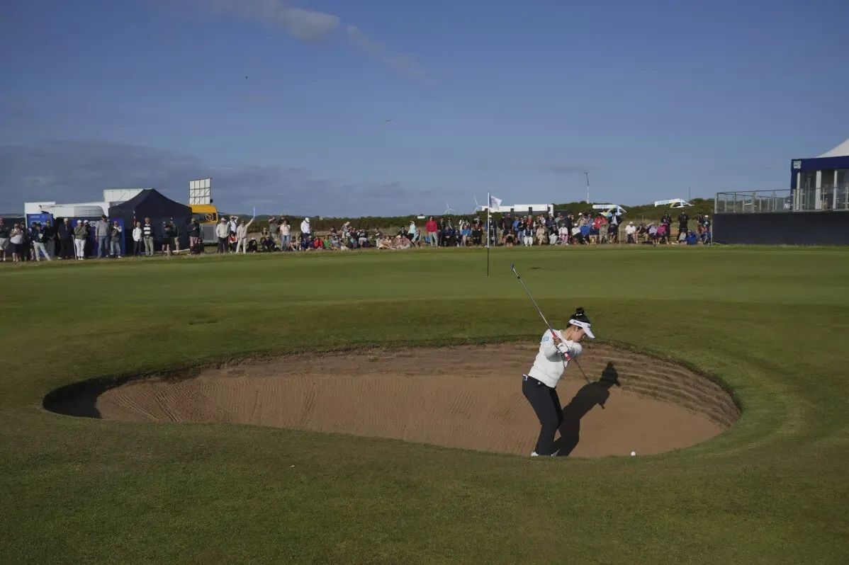 لاعبة جولف تسدد كرة من مخبأ رمل أثناء بطولة بريطانيا المفتوحة للسيدات في رويال بورثكاول، مع جمهور كبير في الخلفية.