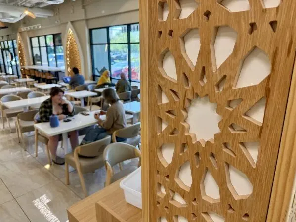 تصميم داخلي لمقهى يمني، يظهر تفاصيل هندسية مستوحاة من العمارة الإسلامية، مع زبائن يستمتعون بمشروباتهم في أجواء مريحة.