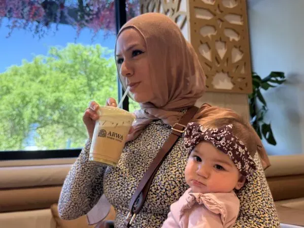 امرأة ترتدي الحجاب تحتسي مشروب قهوة من مقهى Arwa، بينما تحمل طفلة صغيرة. تعكس الصورة تجربة القهوة اليمنية في الأجواء الاجتماعية.