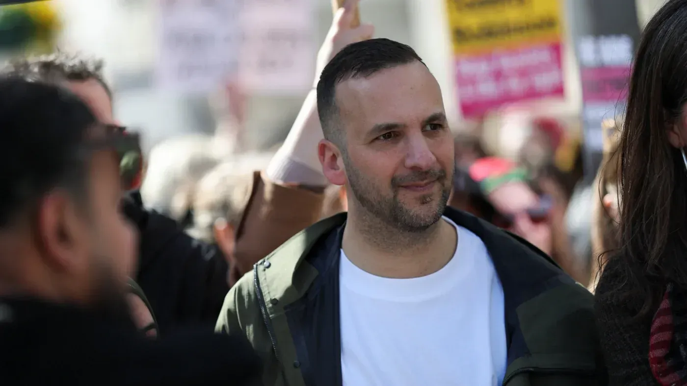 زعيم حزب الخضر زاك بولانسكي في تجمع عام، محاط بجمهور يحمل لافتات، يعبر عن قضايا سياسية واجتماعية مهمة.