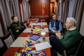 اجتماع ثلاثي في غرفة مغلقة، حيث يناقش المشاركون القضايا السياسية، مع وجود فواكه ووجبات خفيفة على الطاولة.