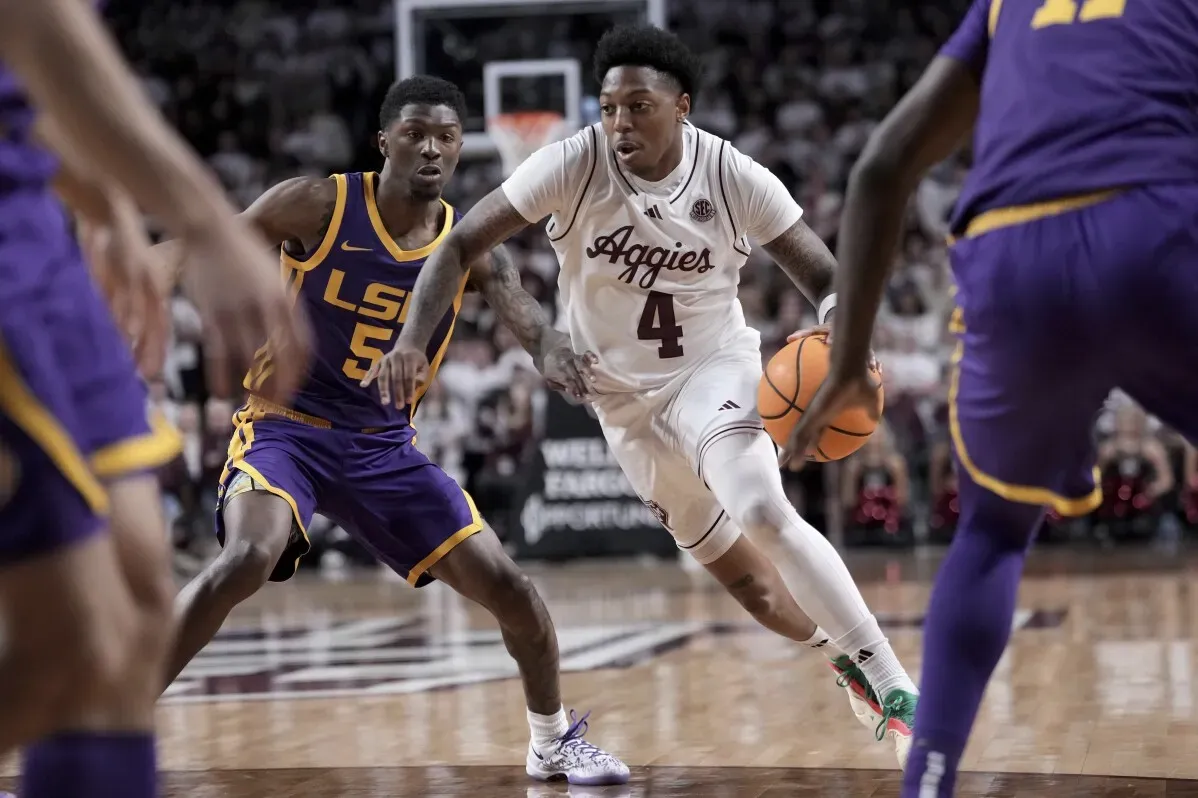 لاعب كرة السلة رقم 4 من تكساس إيه آند إم يتقدم بالكرة أثناء مواجهة لاعب LSU في مباراة كرة سلة، مع وجود جمهور في الخلفية.