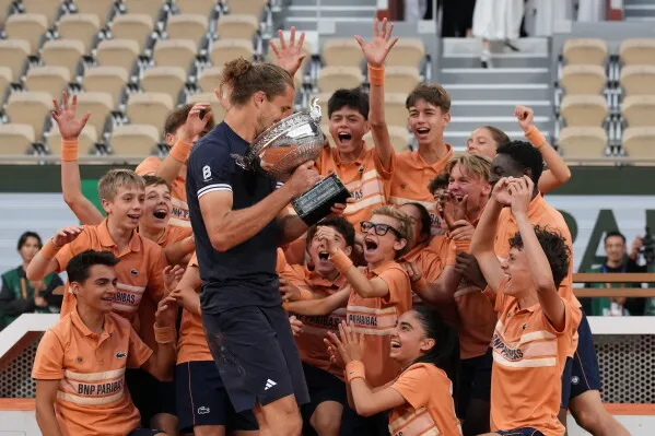 احتفال Alexander Zverev بفوزه ببطولة Roland Garros وسط مجموعة من الأطفال المبهجين، حيث يحمل الكأس مع تعبيرات الفرح.